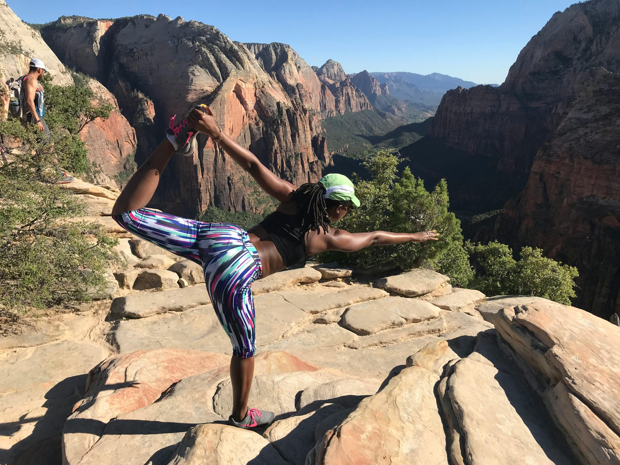 A woman performs a yoga pose on a mountain peak surrounded by stunning natural landscapes.