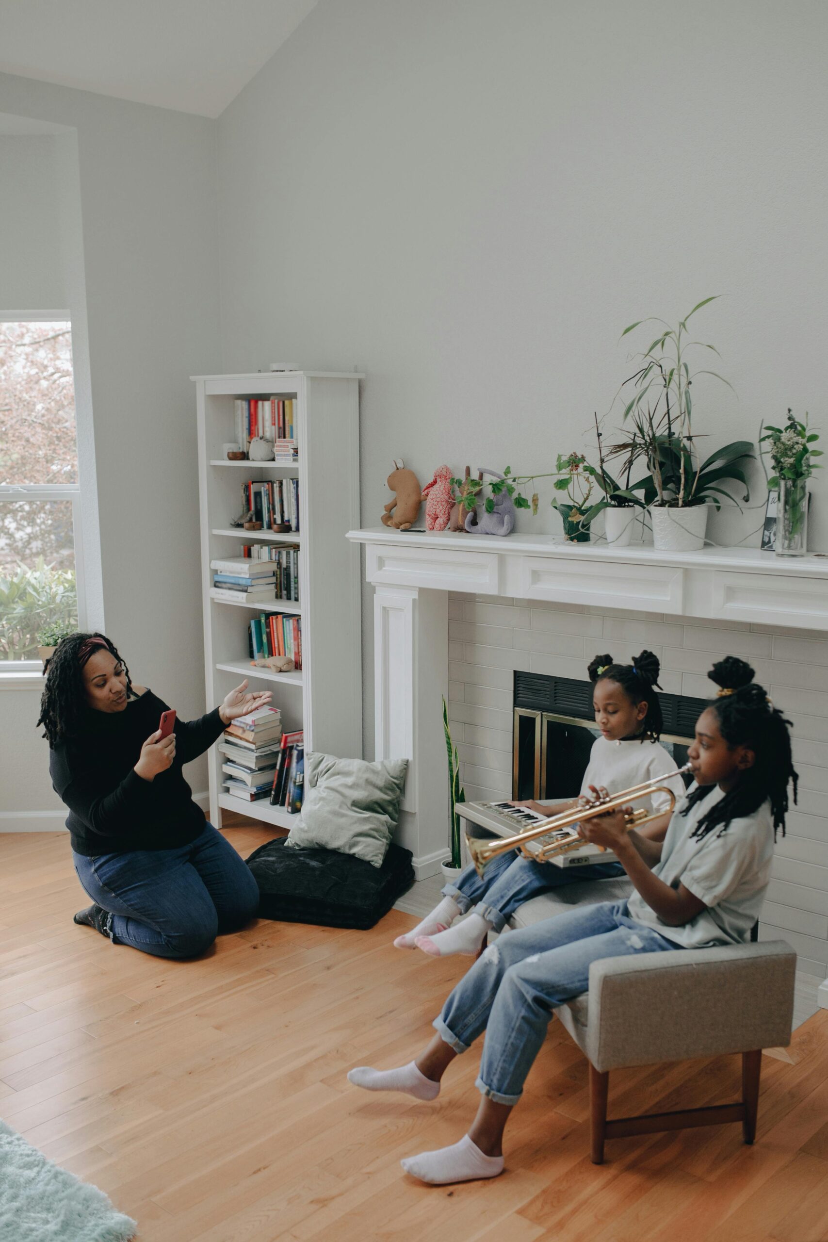 Mother films daughters practicing trumpet at home. Warm family moment.