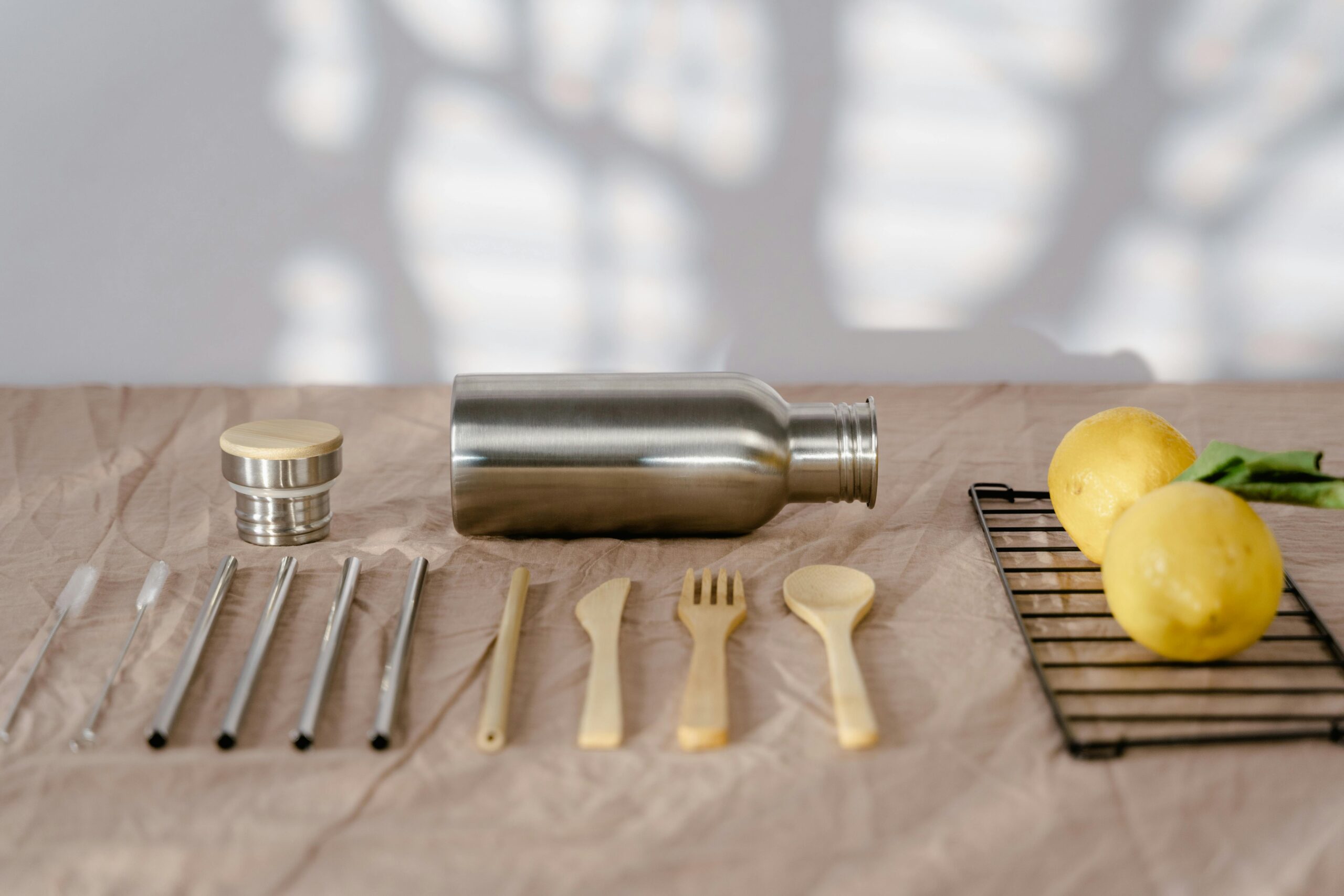 Zero waste setup with a metal water bottle, reusable cutlery, and lemons in a warm setting.