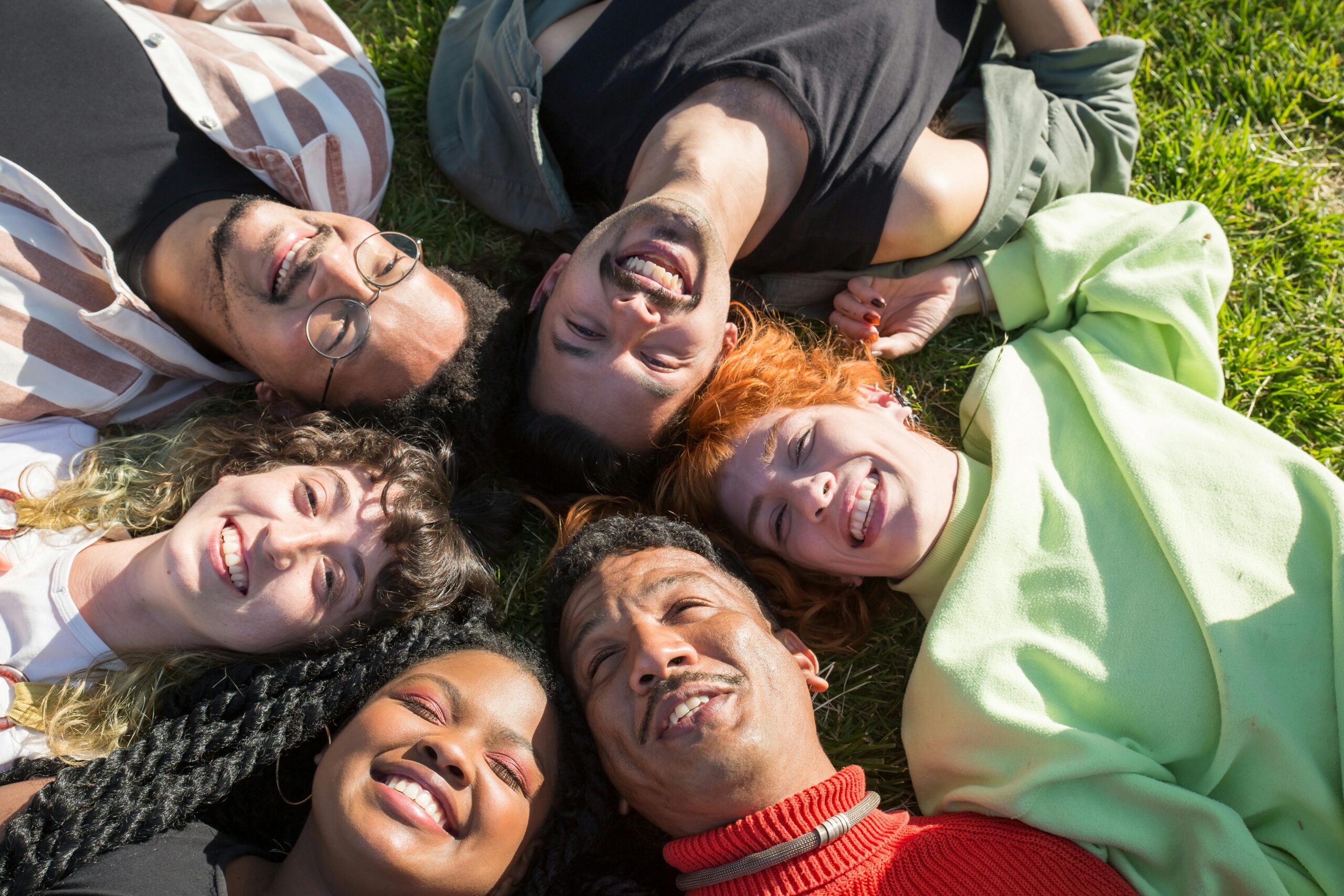 A joyful group of diverse friends lying on grass, smiling and enjoying a sunny day in Portugal.